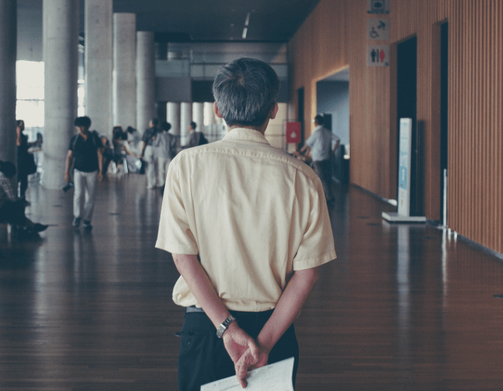 A Man holding a paper behind his back looking at a hallway with students in it